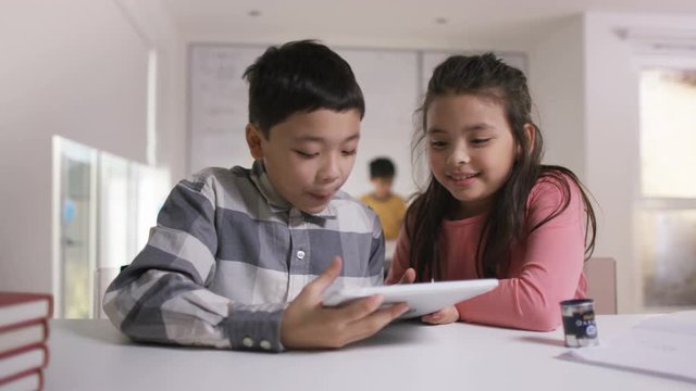  Happy little boy & girl working on computer tablet in school classroom