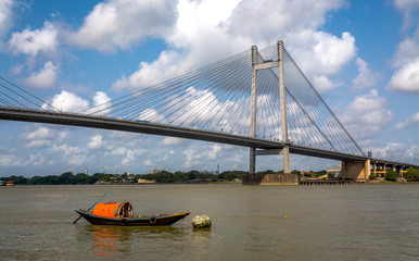 Solitary wooden boat on the river Hooghly overlooking the Vidyasagar Setu bridge. Photograph taken from Princep ghat Kolkata, India.