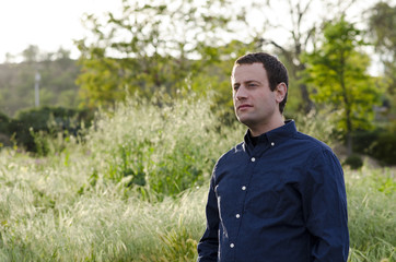 Optimistic man outdoors in a grassy field thinking of what tomorrow will bring. 