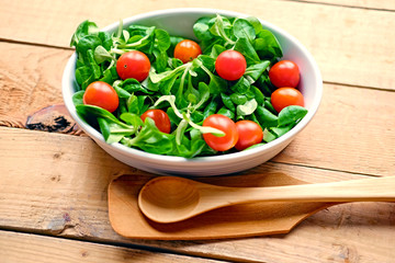 Cherry tomatoes and basil salad in a white cup on a wooden table.