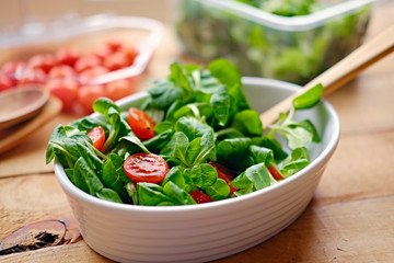 Cherry tomatoes and basil salad on a plate with a pot on a wooden table.
