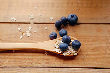 Wooden spoon with oat flakes and blueberry over wooden pattern background.