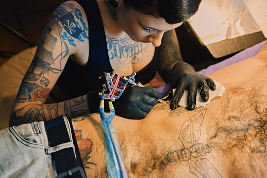 Close up image of female tattoo artist makes a tattoo on a man's torso.