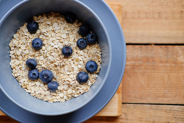 Oat flakes with blueberry in a blue cup on a wooden table.