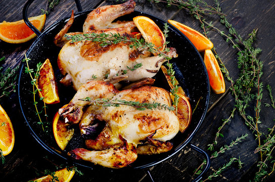 Roasted two chicken with oranges and thyme on dark wooden background.