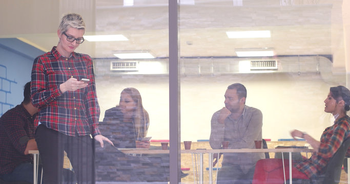 Business Woman Looking Through A Window And Using On A Cell Phone During Bussines Meeting