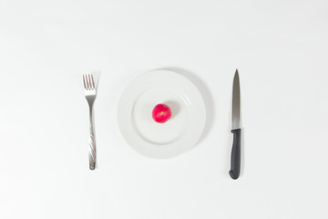 One red radish on white plate on white background with fork and knife.