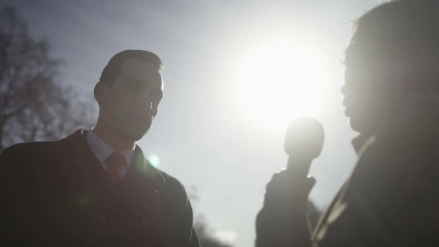  Man in business dress giving live interview to reporter outdoors in city