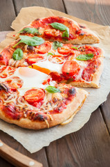 Homemade pizza with tomato sauce cheese egg and basil leaves served on wooden table. Top view
