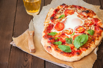Homemade pizza with tomato sauce, cheese, egg and basil leaves beer served on wooden table. Top view