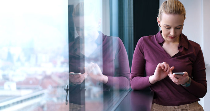 Elegant Woman Using Mobile Phone by window in office building