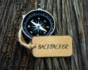 Compass and paper tag written with BACKPACKER on wooden background.