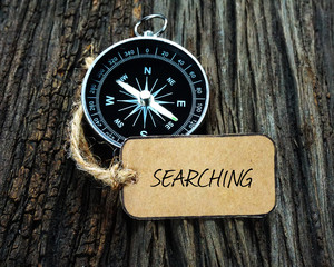 Compass and paper tag written with SEARCHING on wooden background.