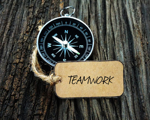 Compass and paper tag written with TEAMWORK on wooden background.