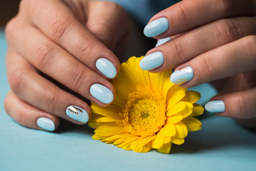 Girl with blue manicure holds a yellow flower