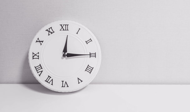 Closeup white clock for decorate show a quarter past twelve o'clock or 12:15 p.m. on white wood desk and wallpaper textured background in black and white tone with copy space
