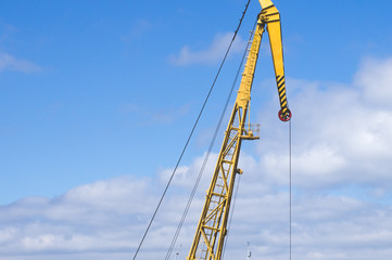 Naklejka premium Yellow arrow of the port crane against the blue sky and clouds. River port equipment for unloading ships and barges