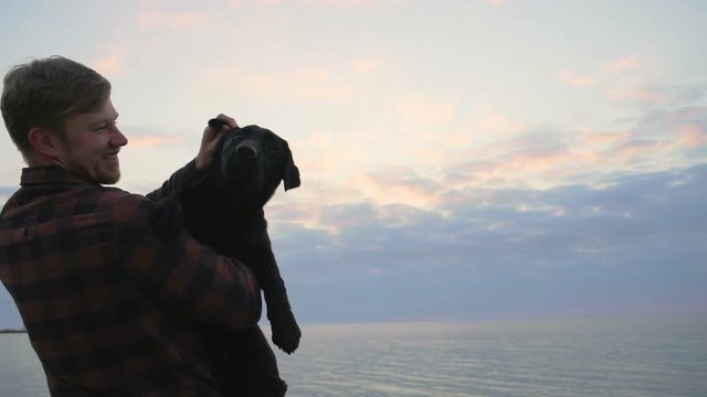 Young male hugs his dog near at sea and play with him slow motion