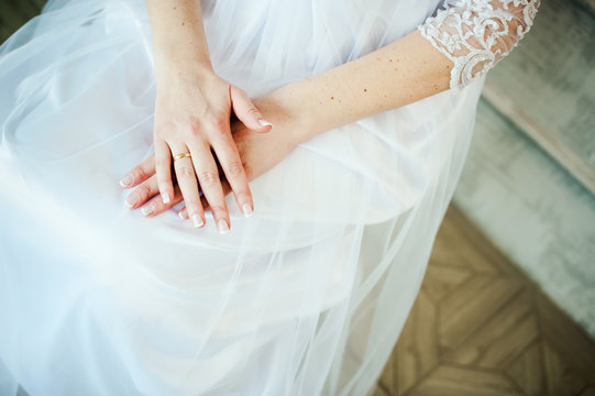 bride in a wedding dress folded her hands on her knees, an engagement ring on her finger