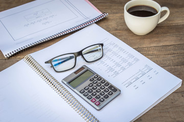 Calculator, notepad, eyeglasses and cup of coffee, on wooden background. business still life