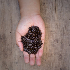 Coffee beans in hands on wooden background