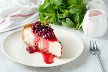 Slice of cheesecake with sour cherry sauce and fresh mint on white plate