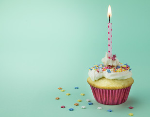 One cupcake with lit candle and star sprinkles isolated on green background