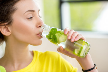 Close-up of a woman drinking water with mint, cucumber and lime during a workout with dumbbells....