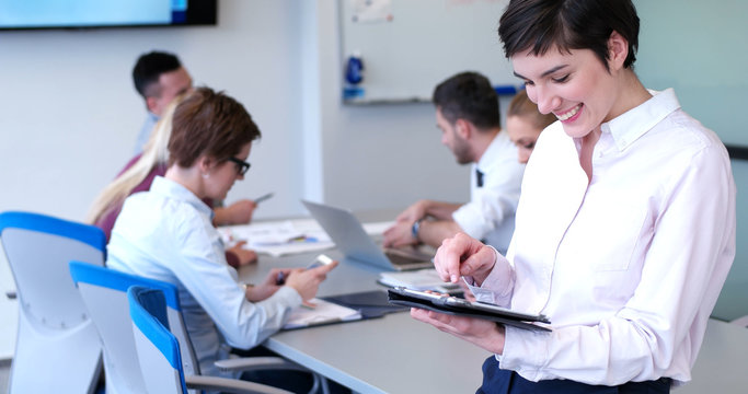 Portrait of  smiling casual businesswoman using tablet  with coworkers standing in background