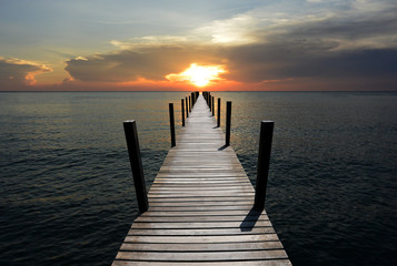 The wooden bridge in the sea at sunset is beautiful.