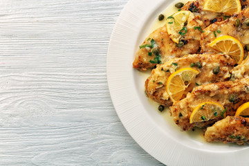 Plate with delicious chicken piccata on wooden table