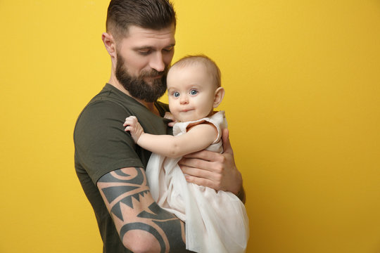 Handsome tattooed young man holding cute little girl on color background