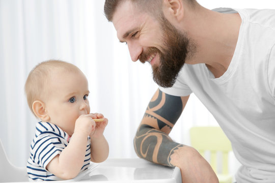 Handsome tattooed young man feeding cute little baby at home