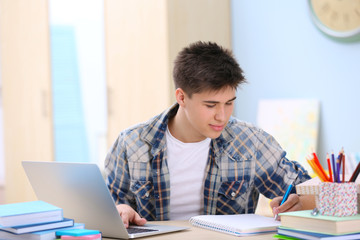 Teenager using laptop and taking notes at home