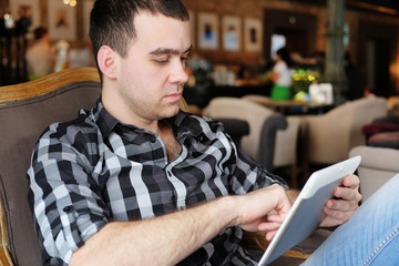 A successful young man in a dark plaid shirt in the cafe does business. Young hipster holding a smartphone, tablet computer. Office worker on lunch. business meeting. send a message.