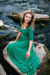 Beautiful girl posing on rocks near the water. Model in a green dress in nature.