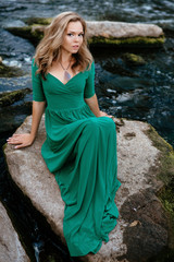 Beautiful girl posing on rocks near the water. Model in a green dress in nature.
