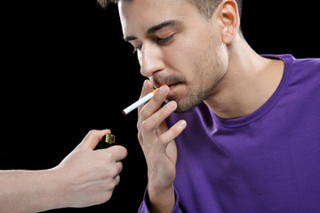 Obraz premium Young man lighting cigarette on black background