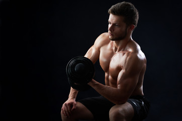 Fototapeta na wymiar Handsome young sportive shirtless man with muscular strong sexy body doing exercises using dumbbell against black background copyspace gym athletics physique sports motivation achievement gaining.