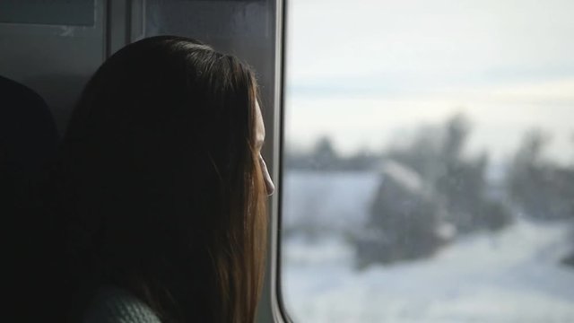 Young woman looking on window during riding on train. Profile of attractive girl traveling on railroad. Slow motion