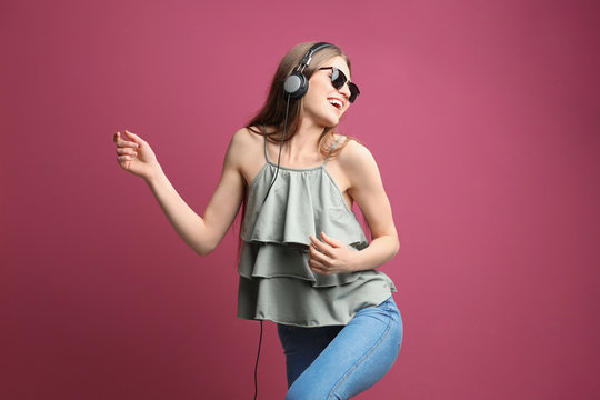 Beautiful young woman in headphones listening to music on color background
