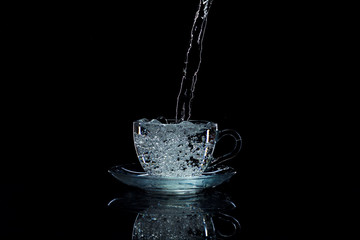 Water pours into a clear glass cup, black background, studio light