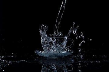 Water pours into a clear glass cup, black background, studio light