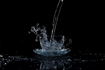 Water pours into a clear glass cup, black background, studio light