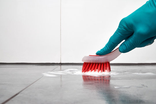 Male hand with red brush cleaning the bathroom tiles on the floor.