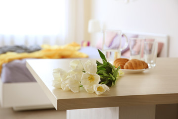 Beautiful bouquet of white tulips and croissants on table in light room
