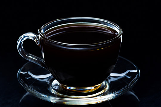 Hot black coffee smokes in a glass cup on a black background, studio light
