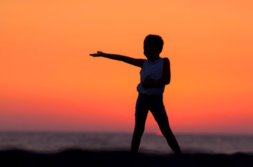 Fototapeta premium A Silhouette Of A Child Playing Near The Beach At Sunset