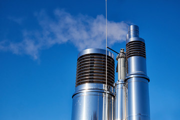 Round ventilation chimneys of polished stainless steel with slats sending out vapor on a clear blue sky