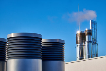 Round ventilation chimneys of stainless steel on the roof of a low white building facade with a wide steel door